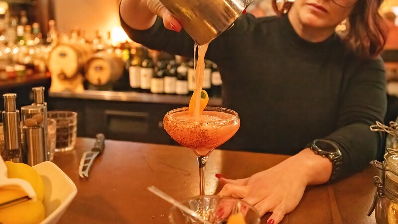 Bar tender pouring cocktail in glass