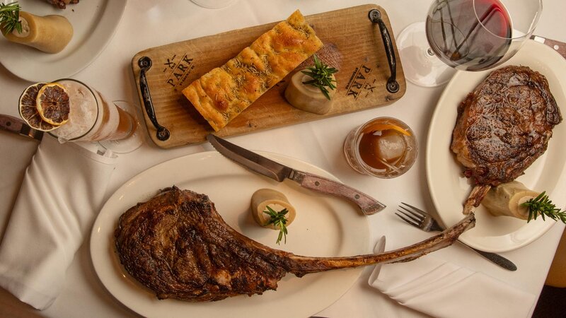 Top down view of plated steaks, cocktails and bread